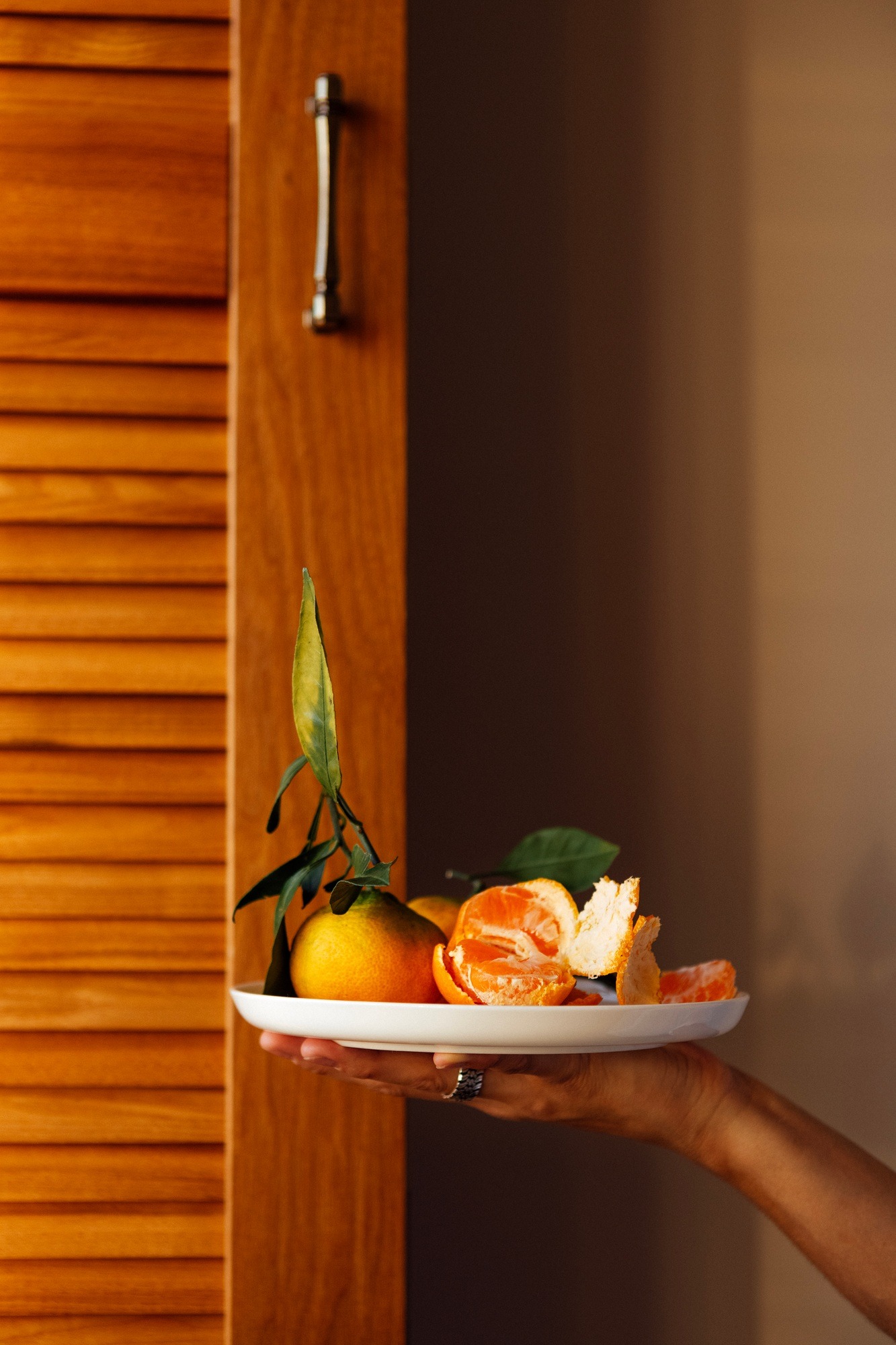 A close-up of a female hand with a ceramic white plate with juicy tangerines