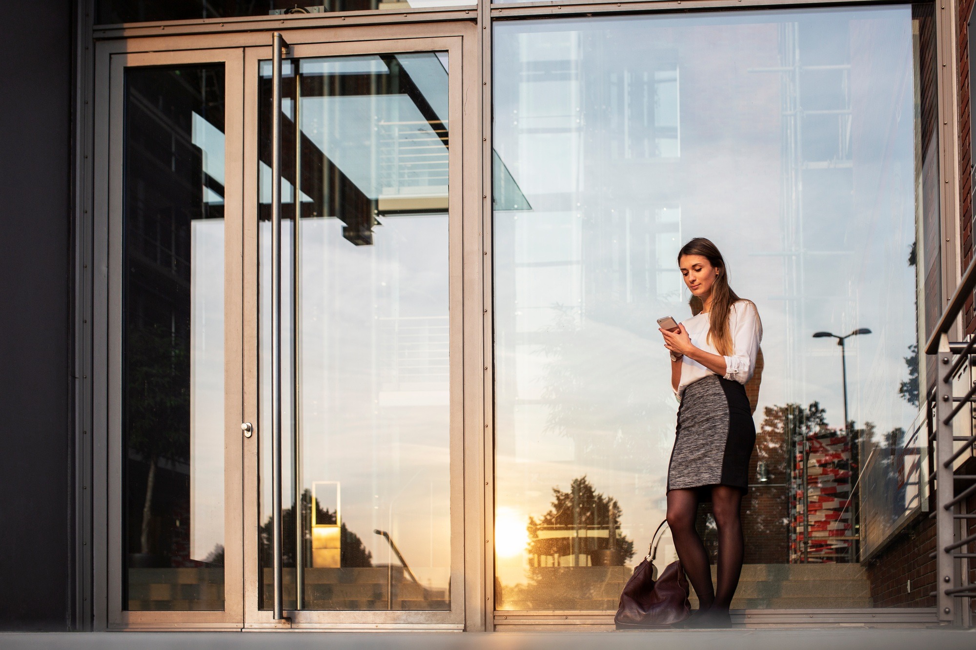Woman standing against glass door and using smart phone